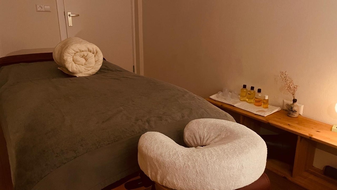 Massagetafel met hoofdsteun in warm licht, een bijzettafel met olie en een vaasje